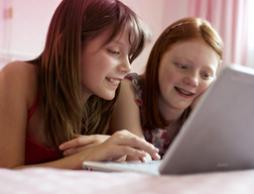 Bild på två unga flickor som sitter framför en dator. Bilden illustrerar att det är vanligt att ha många frågor, och på o.b.®'s hemsida kan du hitta information om den första mensen, puberteten och annan bra information