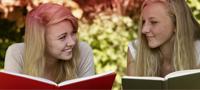 Bild på två unga kvinnor som läser vars en bok. Bilden illustrerar de många myter det finns i samband med menstruation.